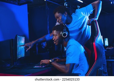 Trainer explains strategy for team play in online video game. Cyber coach training African man for esports. - Shutterstock ID 2256025133