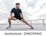 A trainer in fitness clothes is a T-shirt, running sports shoes and a smart watch for sports.    A strong man. A confident male athlete training does warm-up exercises.