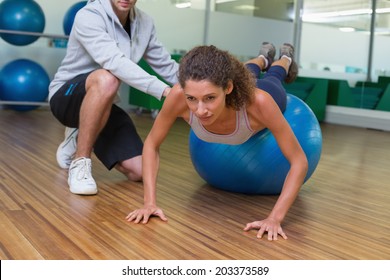 Trainer helping his client doing push up on exercise ball at the gym