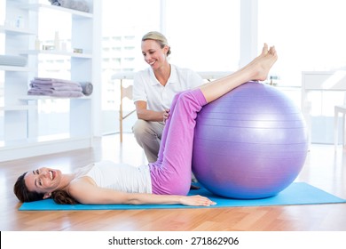 Trainer Helping Woman With Exercise Ball In Medical Office