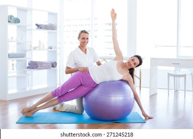 Trainer Helping Woman On Exercise Ball In Medical Office