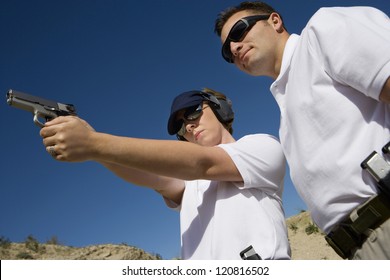 Trainer helping young woman to aim with handgun at combat training