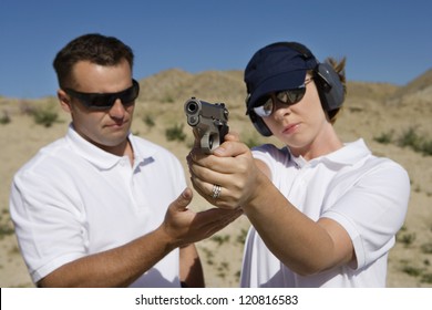 Trainer Helping Young Woman To Aim With Handgun At Combat Training