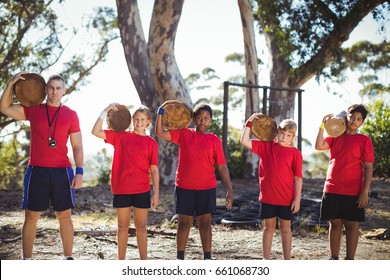 Trainer and kids carrying wooden logs during obstacle course training in the boot camp - Powered by Shutterstock