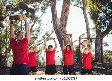 Trainer and kids carrying wooden logs during obstacle course training in the boot camp - Powered by Shutterstock