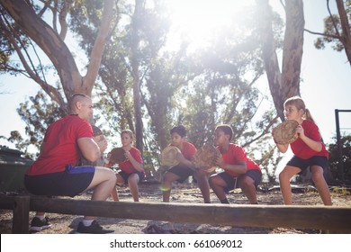 Trainer and kids carrying wooden logs during obstacle course training in the boot camp - Powered by Shutterstock