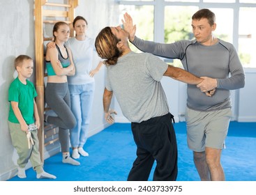 Trainer and man in group self-defense classes practicing sparring technique of blowing to chin in gym, in background family watches of performing technique - Powered by Shutterstock