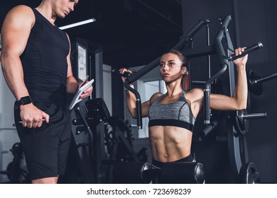 trainer with notebook checking woman training in gym - Shutterstock ID 723698239