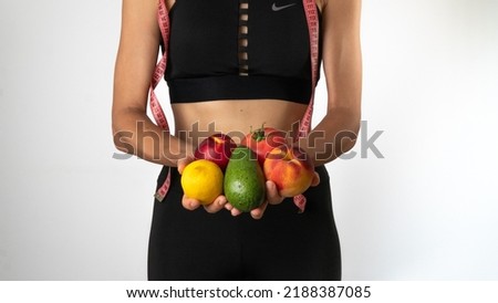 Trainer nutritionist woman holds fruits and vegetables in her hands, measuring tape on the neck - sports, weight loss and proper nutrition