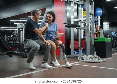 A trainer person with prosthetic leg,holding digital tablet,doing fist bump with senior client after finished discussing workout program design,concept of health,exercise,athlete - Powered by Shutterstock