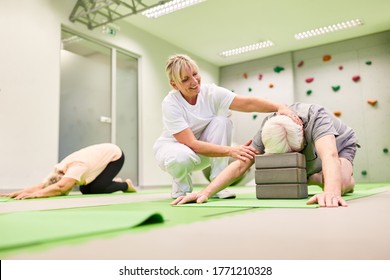 Trainer or physiotherapist cares for seniors during back training with the yoga block - Powered by Shutterstock