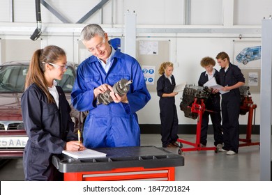 A trainer practically showing and teaching an auto part to a student in a vocational school of automotive trade with other students working in the back ground - Shutterstock ID 1847201824