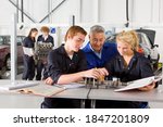 A trainer sitting in the middle of two young students while teaching them about automobile part in a vocational school of automotive trade