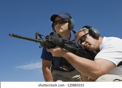 Trainer standing with mature man aiming with gun