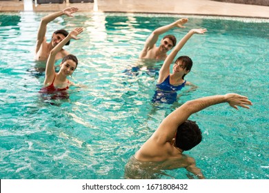 Trainer working out with smiling people during water aerobics in swimming pool