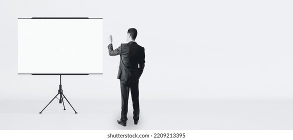 Training And Business Seminar Concept With Man In Black Suit Back View In Front Of Blank White Flip Chart With Place For Your Logo Or Text On Light Wall Background, Mock Up