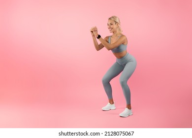 Training For Glute Muscles. Smiling Fit Young Lady In Bright Yellow Sportswear Doing Deep Squat Exercise During Workout, Warming Up, Isolated On Pink Studio Wall. Full Body Length Banner, Mockup