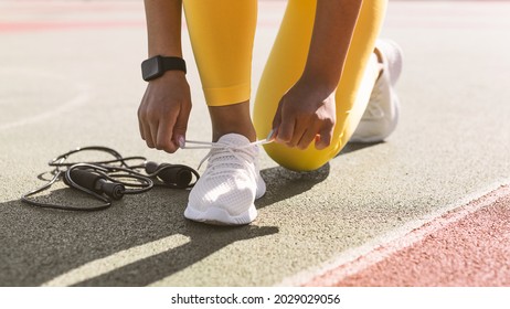 Training, Healthy Lifestyle Concept. Closeup cropped view of unrecognizable African American woman in yellow leggings tying her shoelaces before jogging outdoors in the morning, wearing white sneakers
