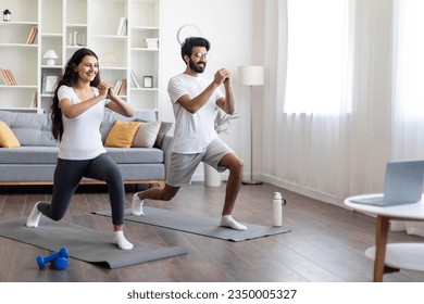 Training At Home. Sporty indian couple doing glutes exercise in front of laptop, happy young eastern spouses watching online tutorials and exercising in living room, practicing sports together - Powered by Shutterstock