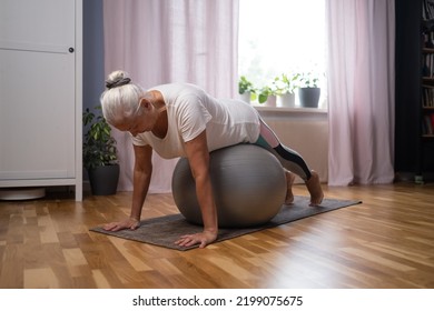 Training At Home. Sporty Senior Woman Doing Yoga Plank Using A Ball Exercising In Living Room