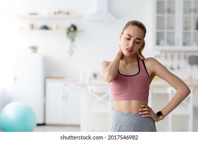 Training Injury, Suffering From Pain And Health Problems At Home Alone. Sad Unhappy Millennial Attractive Blonde Female Athlete In Sportswear Rubs Neck, On Kitchen Interior Background, Empty Space