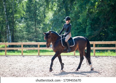 Training process. Young teenage girl riding bay trotting horse on sandy arena practicing at equestrian school. Colored outdoors horizontal summertime image with filter