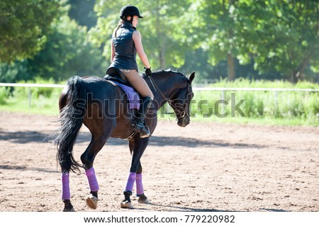 Training process. Young teenage girl riding a horse on arena at equestrian school. Colored outdoors horizontal summertime image. View from backside.