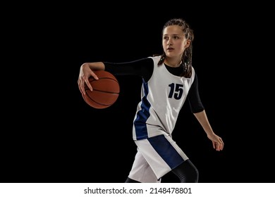 Training. Studio Shot Of Teen Girl In White Uniform Playing Basketball, Doing Dribbling Exercise Isolated Over Black Background. Concept Of Sport, Active Lifestyle, Health, Team Game And Ad