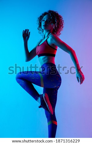 Training. Young sportive woman training isolated on gradient blue-pink studio background in neon light. athletic and graceful. Modern sport, action, motion, youth concept. Beautiful female practicing.
