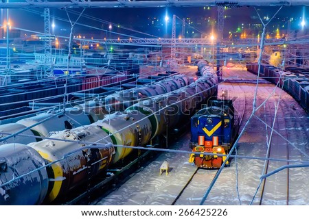 Trains of oil tanks and wagons on the cargo railway station at winter night