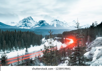 Trains race around a curvy rail road track that snakes alone a frozen river below towering snow capped peaks - Powered by Shutterstock