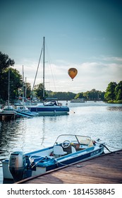 TRAKAI, LITHUANIA - Aug 03, 2020: Vertical Shot Of Boats Standing By A Dock On A Lake Near Trakai Castle With Hot Air Baloon Flying By