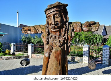 Trakenai, Lithuania - 06.21.2014: A Fabulous Brown Figure Of An Old Man Made Of Wood With Two Barrels In A Roadside Cafe Near Traken, A Blue Sky In The Summer During The Daytime.