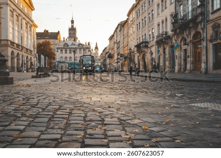 Tram approaching through an old cobblestone street in the historic center of Lviv, Ukraine, surrounded by classic buildings and autumn leaves.