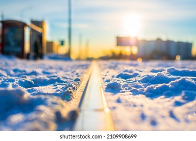 Tram Stop In The City. Sunrise On A Winter Morning. Snow-covered Road. Focus On Tram Tracks. Close Up View From Ground Level.