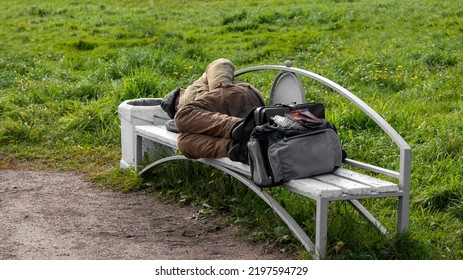 A tramp is lying on a park bench. A tired refugee. Background picture. - Shutterstock ID 2197594729