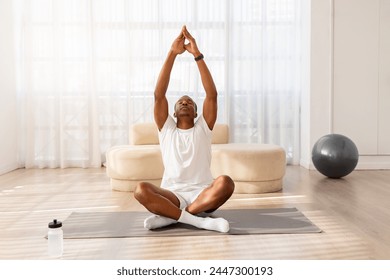 Tranquil African American man in comfortable athletic wear meditates on a yoga mat in a minimalist room - Powered by Shutterstock