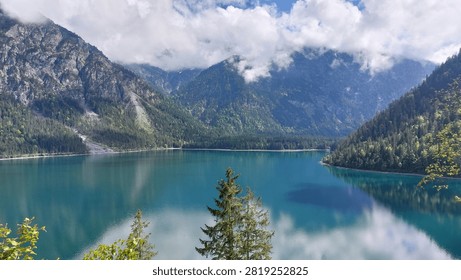 Tranquil Alpine Lake Surrounded by Forested Mountains and Cloud-Capped Peaks Reflected in Turquoise Water