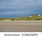 A tranquil beach house behind grassy dunes under a dramatic sky in Thurso, Caithness, Scotland, perfect for serene escapes.