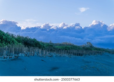 A tranquil beach stretches towards a dramatic sky, where a massive cloud formation dominates the horizon. Zhuangwei Township, Yilan County, Taiwan.