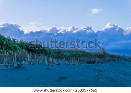 A tranquil beach stretches towards a dramatic sky, where a massive cloud formation dominates the horizon. Zhuangwei Township, Yilan County, Taiwan.