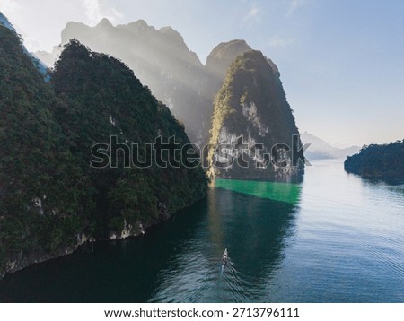 A tranquil boat glides through the pristine waters of Cheow Lan Lake, surrounded by stunning limestone cliffs and vibrant greenery. Khao Sok, Thailand