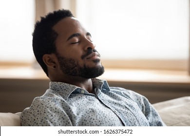 Tranquil calm young african american man resting with eyes closed taking deep breath of fresh air enjoy comfort relaxing on couch feel peace mind and stress relief meditate at quiet home sit on sofa - Powered by Shutterstock