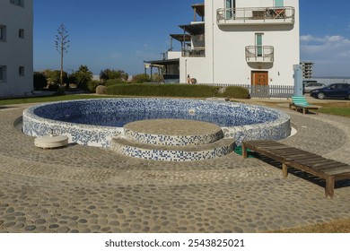 A tranquil circular pool sits near modern architecture, inviting relaxation under a clear blue sky. - Powered by Shutterstock