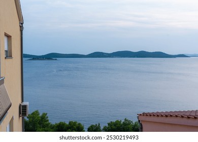 Tranquil coastal landscape with calm sea, distant green islands and residential homes overlooking the water at sunset. High quality illustration - Powered by Shutterstock