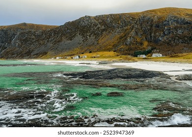 A tranquil coastal landscape features green waters and a rocky shore, with a backdrop of cliffs and autumn foliage. - Powered by Shutterstock