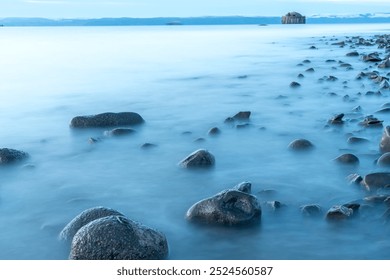 Tranquil Coastal Landscape With Smooth Stones and Calm Waters at Sunrise Near Distant Hut - Powered by Shutterstock