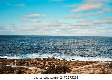 A tranquil coastal road beckons, winding towards a serene blue sea, framed by a partly cloudy sky and distant cliffs, inviting exploration and adventure. - Powered by Shutterstock