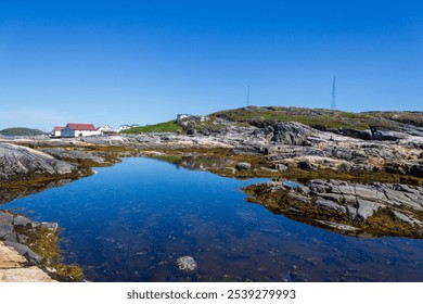 Tranquil coastal scene featuring calm waters, rocky shoreline, and clear blue sky. Remote buildings add rustic charm to the serene environment, evoking feelings of peace and natural beauty. - Powered by Shutterstock