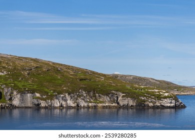 A tranquil coastal scene featuring rocky cliffs and a calm body of water under a clear blue sky, ideal for conveying peacefulness and natural beauty. - Powered by Shutterstock